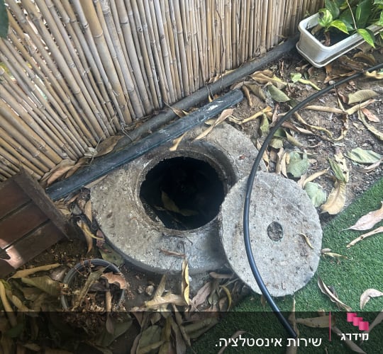 פתח ביוב עם מכסה פתוח ליד גדר במבוק